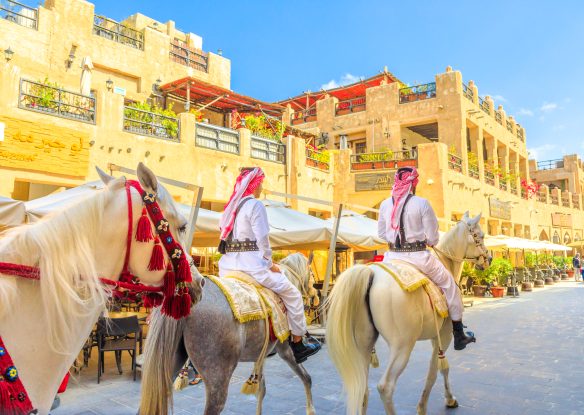 heritage police officers in traditional 1940s Qatari uniform at old Souq Waqif riding white Arabian Horses