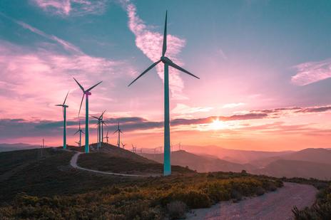 Wind turbines on a hill with winding road and sun setting in the backdrop